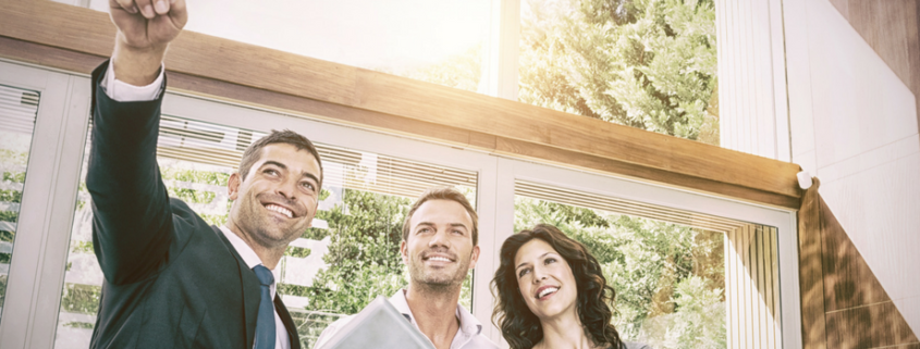 A real estate agent standing with two clients a man and a woman. Smiling and pointing to the house.