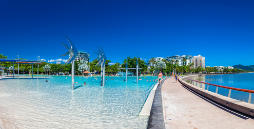 CAIRNS, AUSTRALIA. The Esplanade in Cairns with a jetty and the sea. Palm trees. white sandy beach. With building is the far background.